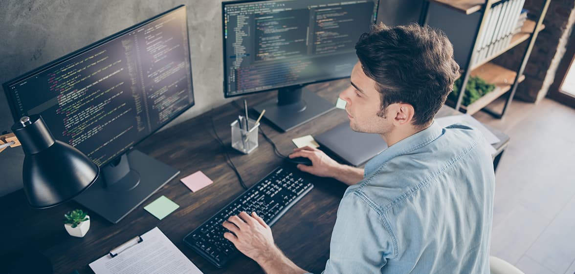 Szoftverfejlesztő Egy programozó ül egy íróasztalnál és két monitor van előtte amin dolgozik.