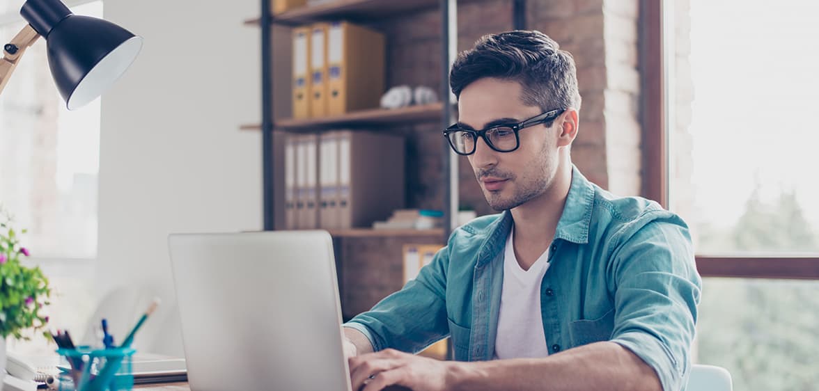 Webfejlesztő Egy szemüveges férfi egy laptop előtt ül egy irodában.